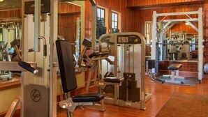 A gym with various exercise machines, wooden floors, and a mirrored wall.