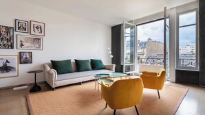 Een moderne woonkamer met een bank, twee fauteuils, een salontafel en kunstwerken aan de wanden.