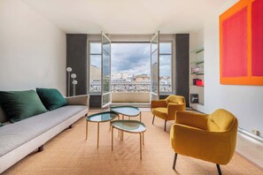Ein modernes Hotelzimmer mit einer Couch, zwei gelben Sesseln, einem kleinen Tisch und einem großen Fenster mit Blick auf die Stadt.