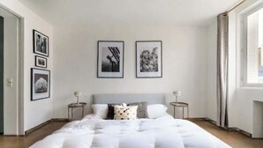 Een slaapkamer met een groot bed, twee nachtkastjes, een raam en drie ingelijste foto’s aan de muur.