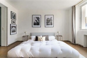 A bedroom with a large bed, two bedside tables, a window, and three framed pictures on the wall.