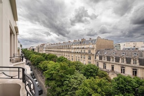 A row of historic buildings with a balcony overlooking a tree-lined street.