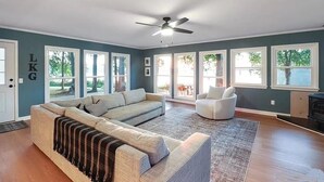 A spacious living room with a large sectional sofa, a white armchair, and a ceiling fan.