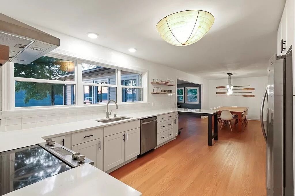 A modern kitchen with white cabinetry, a built-in stove, and a dining area with a wooden table and chairs.