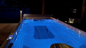A hot tub with a wooden deck surrounding it, equipped with multiple jets and a control panel.