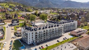A large hotel with multiple floors, a parking lot, and a view of mountains in the background. - Stylish Apartment in Zakopane | Spa Access and Parking (Zakopane)