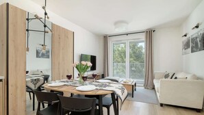 A modern living room with a dining area, wooden walls, a sofa, and a TV. - Stylish Apartment in Zakopane | Spa Access and Parking (Zakopane)