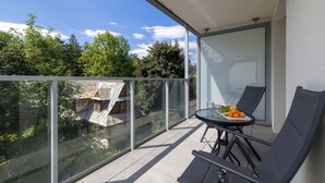 A balcony with a glass railing, a table with chairs, and a view of trees and buildings. - Stylish Apartment in Zakopane | Spa Access and Parking (Zakopane)