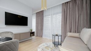 A modern living room with a flat-screen TV, a sofa, a round coffee table, and a small side table. - Practical Studio in Mokotow | Parking | Desk (Warszawa)