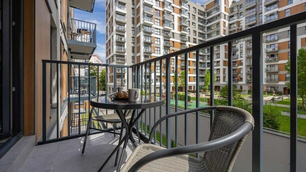 A balcony with a table and chairs, overlooking a residential complex with multiple buildings. - Practical Studio in Mokotow | Parking | Desk (Warszawa)