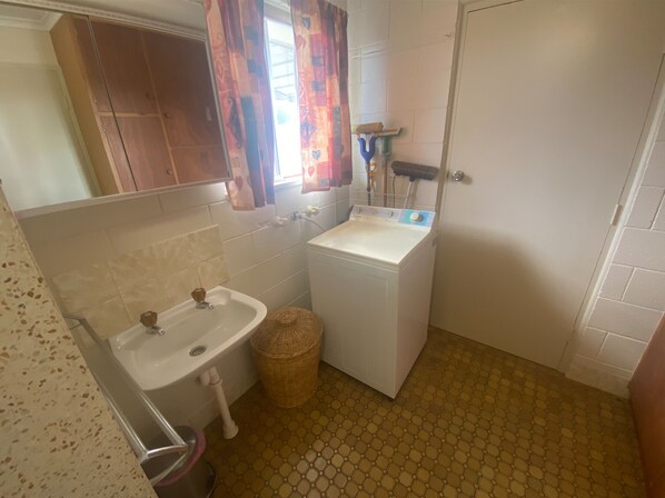 Une petite salle de bain comprenant un lavabo, un lave-linge et une petite poubelle.