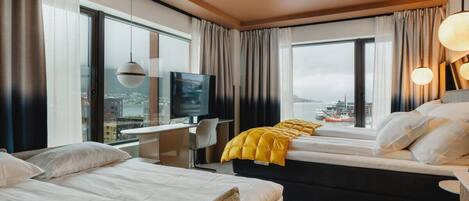 A hotel room with two beds, a desk, a TV, and a large window with a city view.