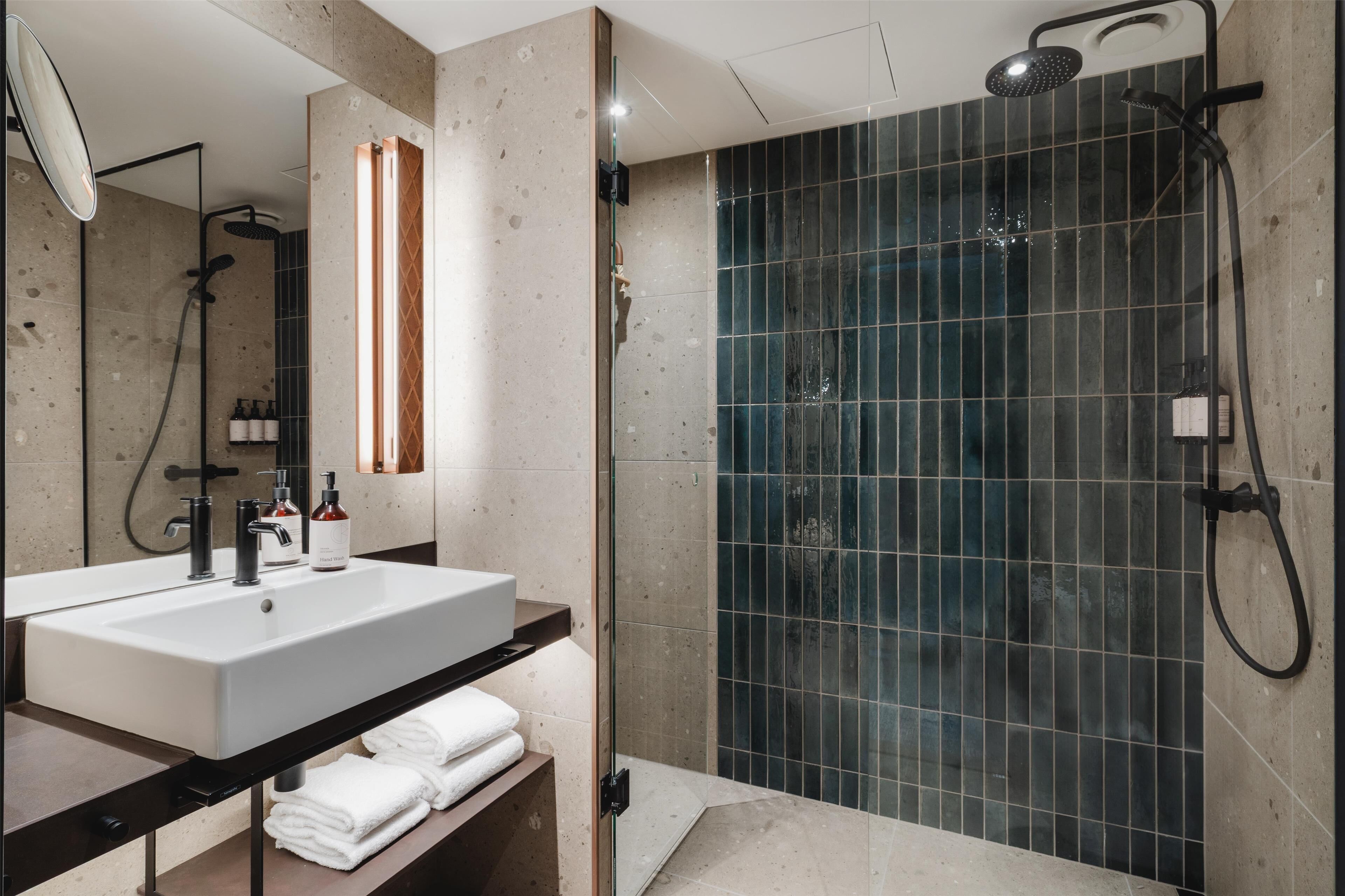 A modern bathroom with a large white sink, a glass-enclosed shower, and a mirror.