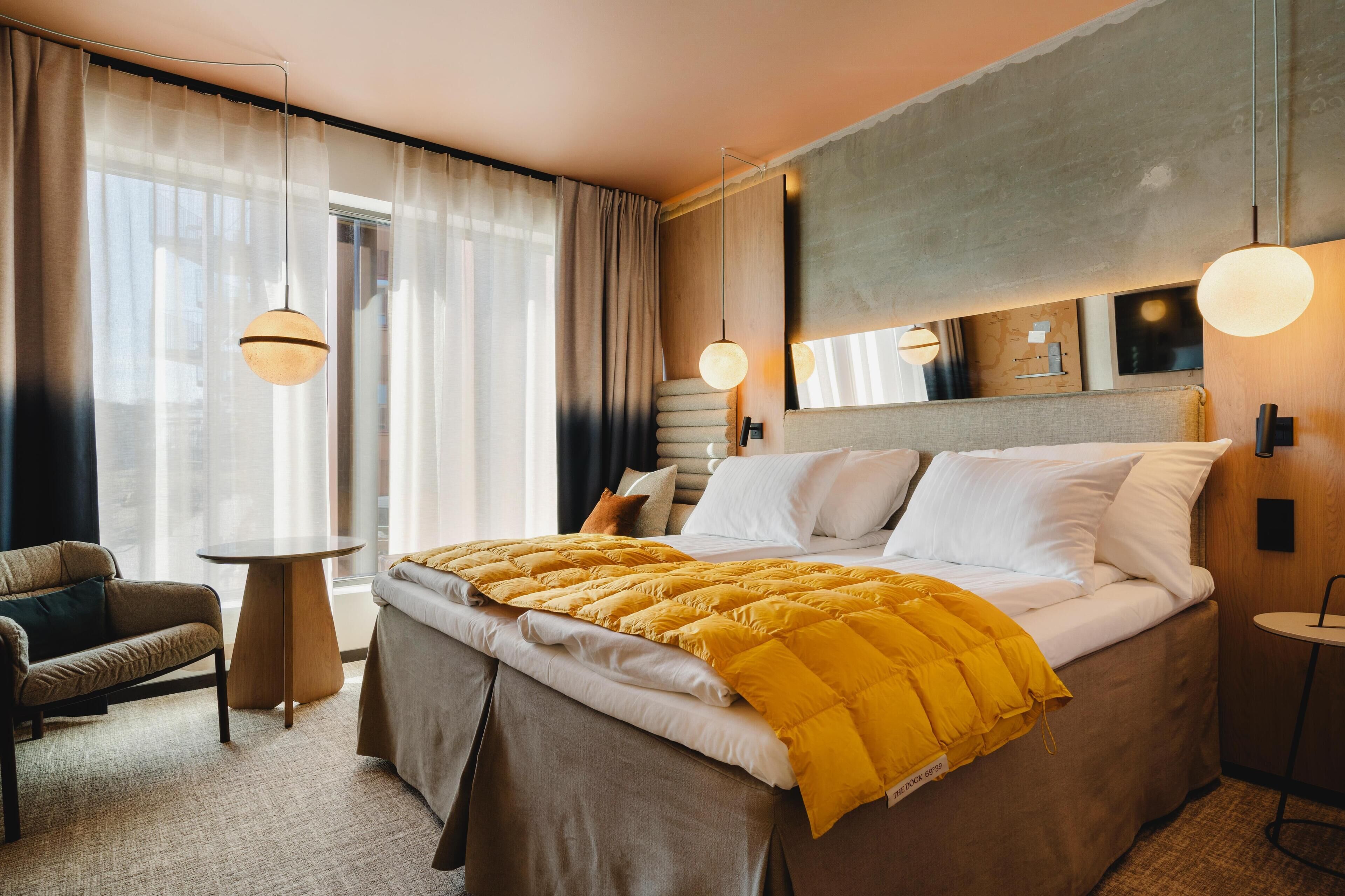 A hotel room with a large bed, a bedside table, a chair, and a window with curtains.