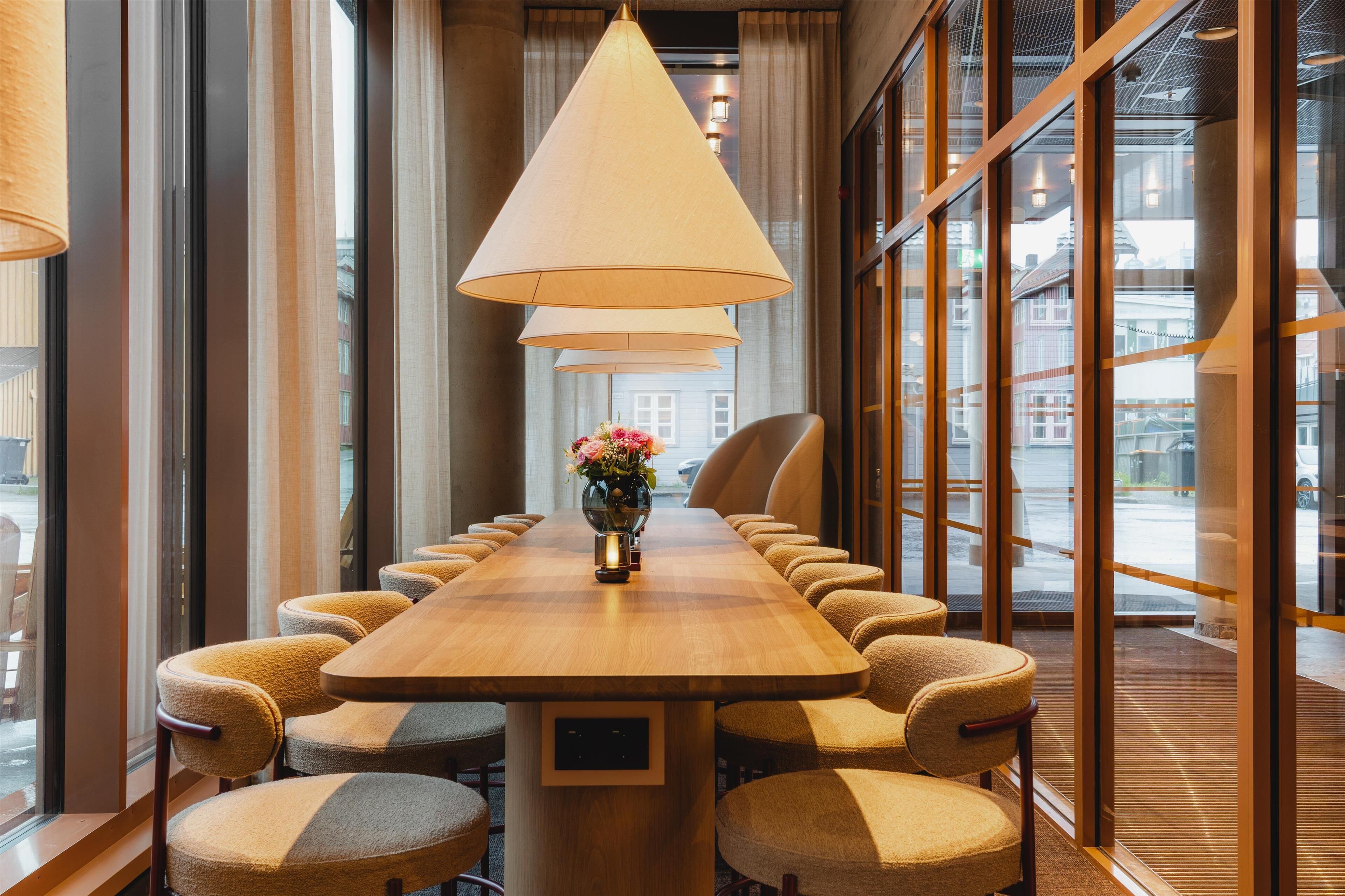Un salón de conferencias con una larga mesa de madera, varias sillas y un jarrón con flores.