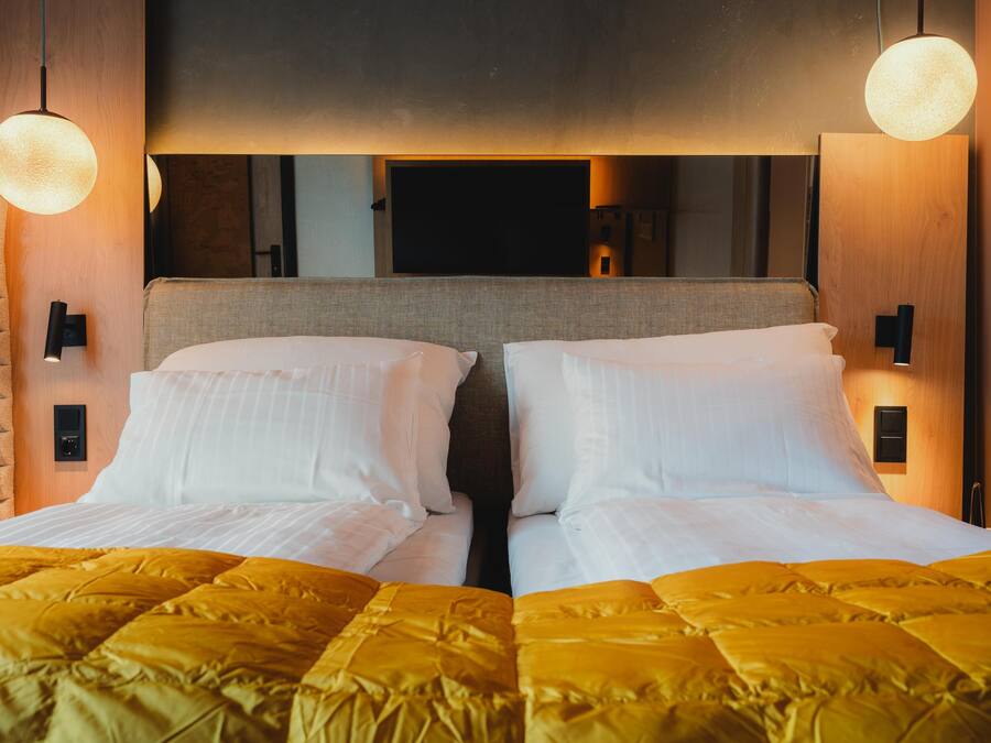 Een tweepersoonsbed met een gele sprei, twee bedlampjes en een grote spiegel boven het bed.