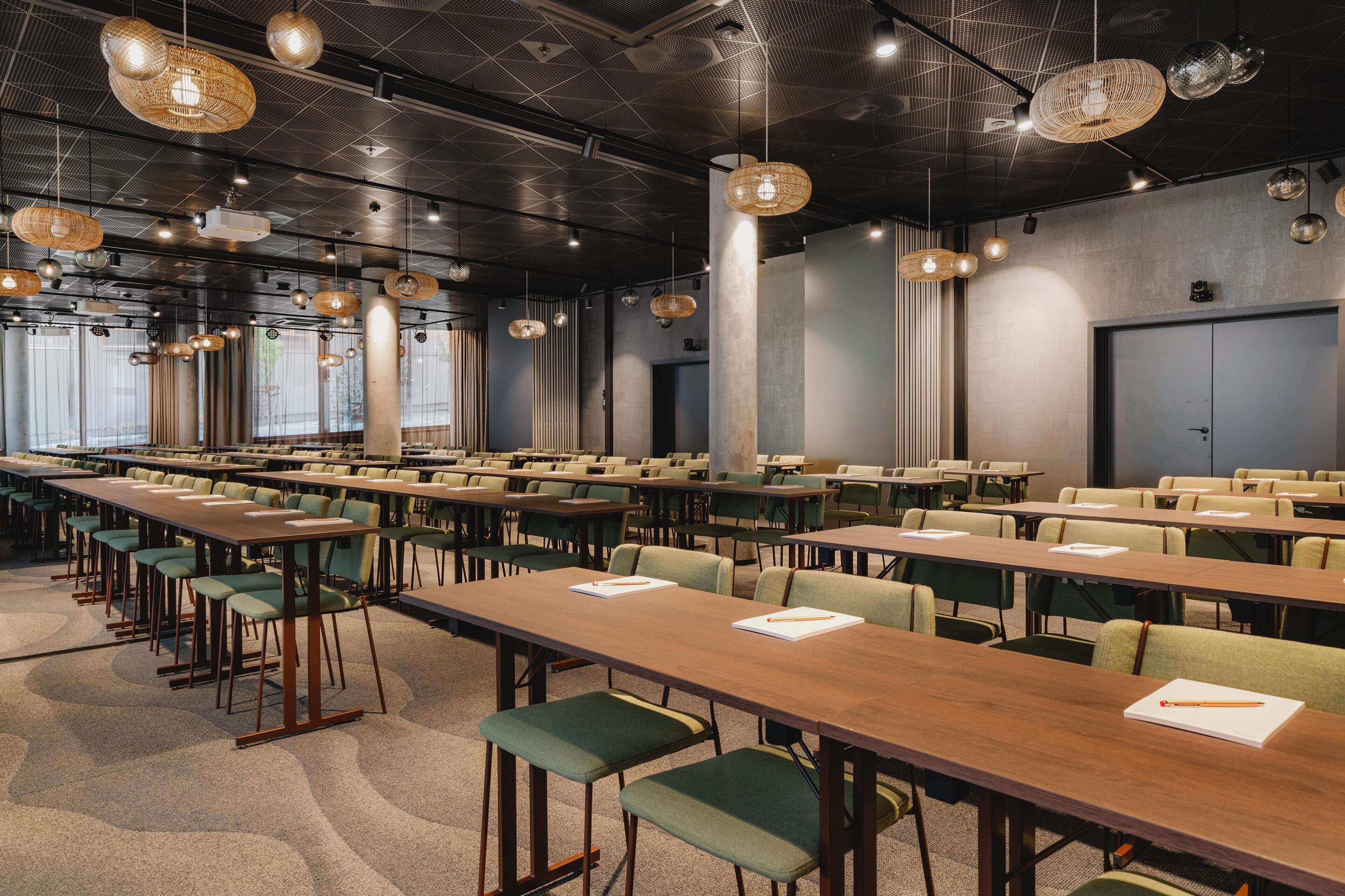 Un salón de conferencias con varias mesas y sillas, ventanas amplias y lámparas colgantes.