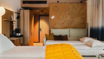 A hotel room with a bed, a desk with a coffee machine, a map on the wall, and a window with curtains.