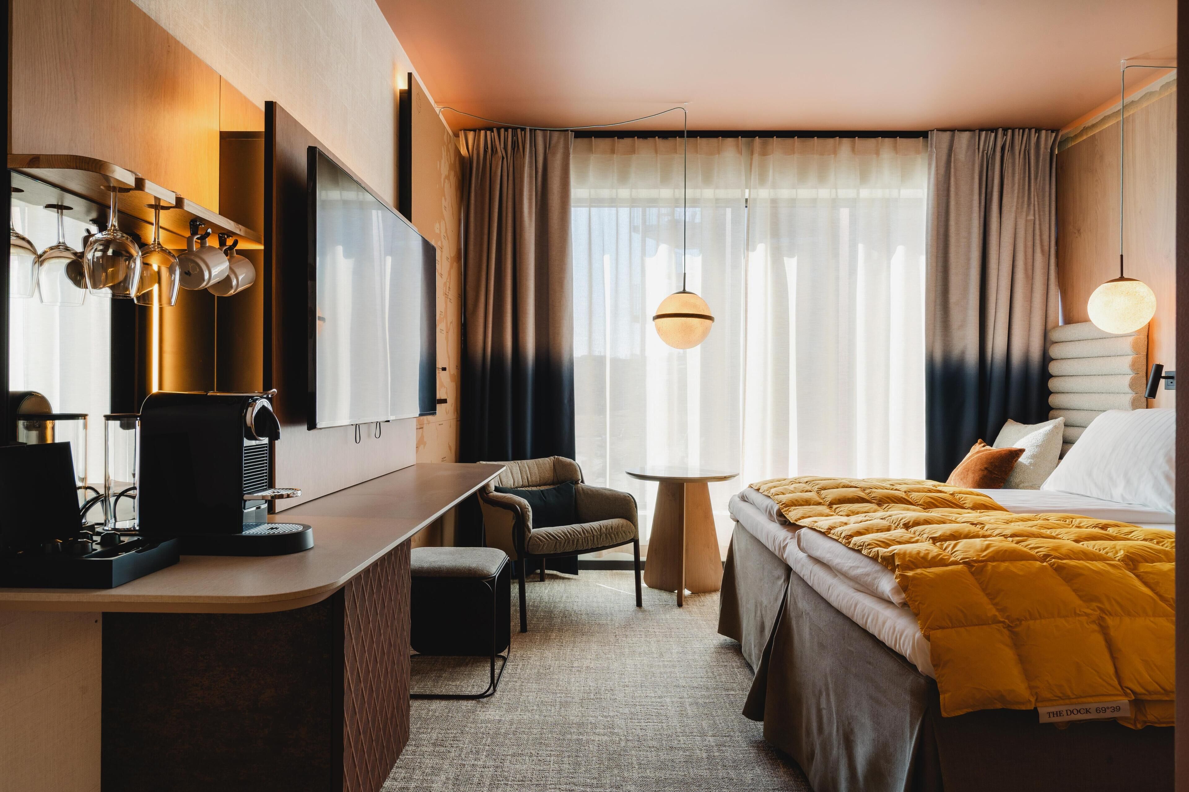 Une chambre d’hôtel comprenant un lit, un bureau avec une machine à café, une télévision, une chaise, une petite table et un luminaire suspendu.