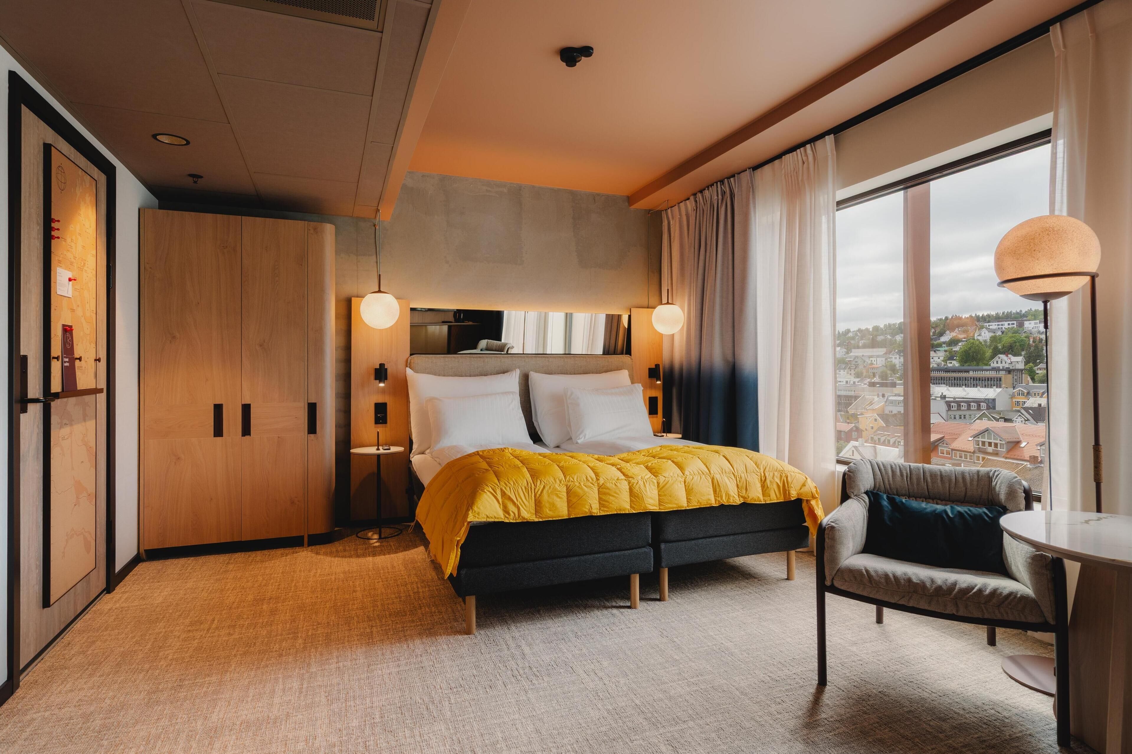 Een moderne hotelkamer met een bed, een stoel, een bureau en een groot raam met uitzicht op de stad.