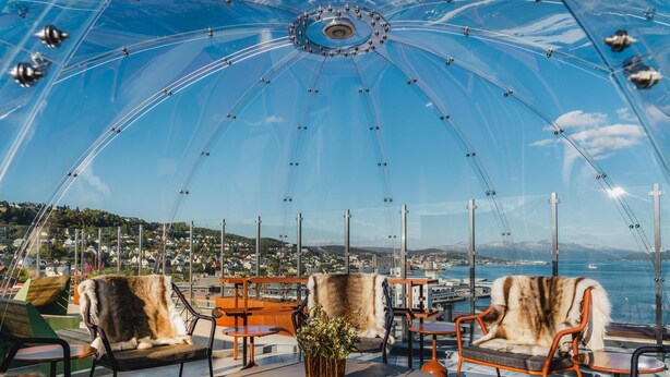 A transparent dome structure with seating and tables, overlooking a coastal cityscape. - The Dock 69°39 by Scandic (Tromsø)
