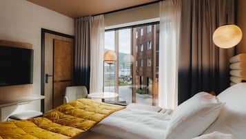 Habitación de hotel con cama, televisión, escritorio, silla, mesita y vistas al exterior.