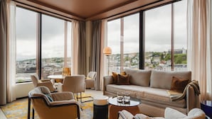 A modern living room with a sofa, chairs, a coffee table, and a view of the city through large windows. - The Dock 69°39 by Scandic (Tromsø)