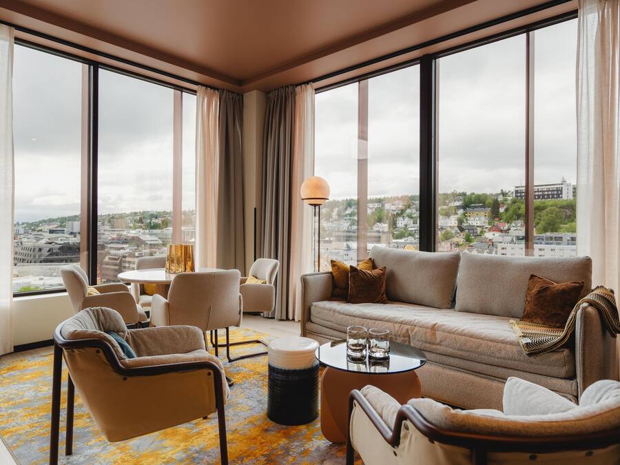 A modern living room with a sofa, chairs, a coffee table, and a view of the city through large windows.