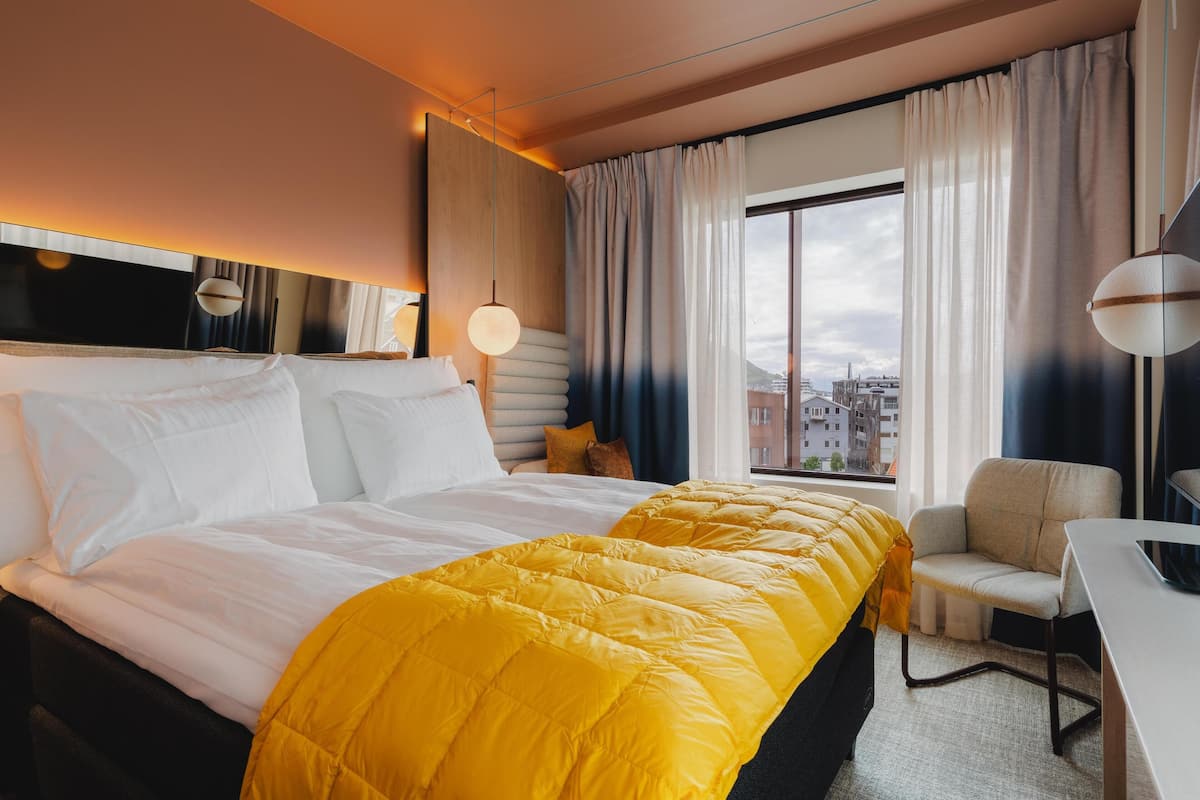 Une chambre d’hôtel avec un grand lit, un bureau, une chaise et une vue sur la ville par la fenêtre.