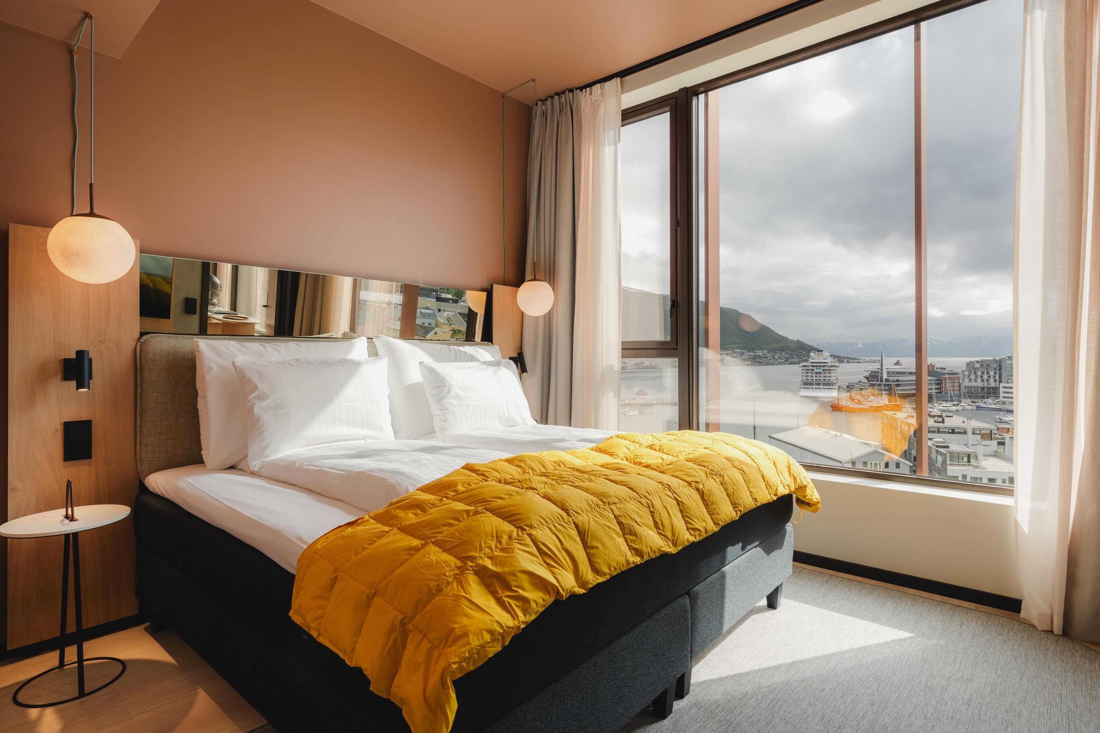 A modern hotel room with a large bed, a view of the city, and a cityscape visible through the window.