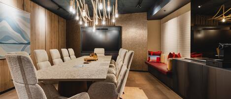 Una sala de conferencias moderna con una larga mesa, sillas cómodas, una pantalla grande y una zona de cocina con asientos.