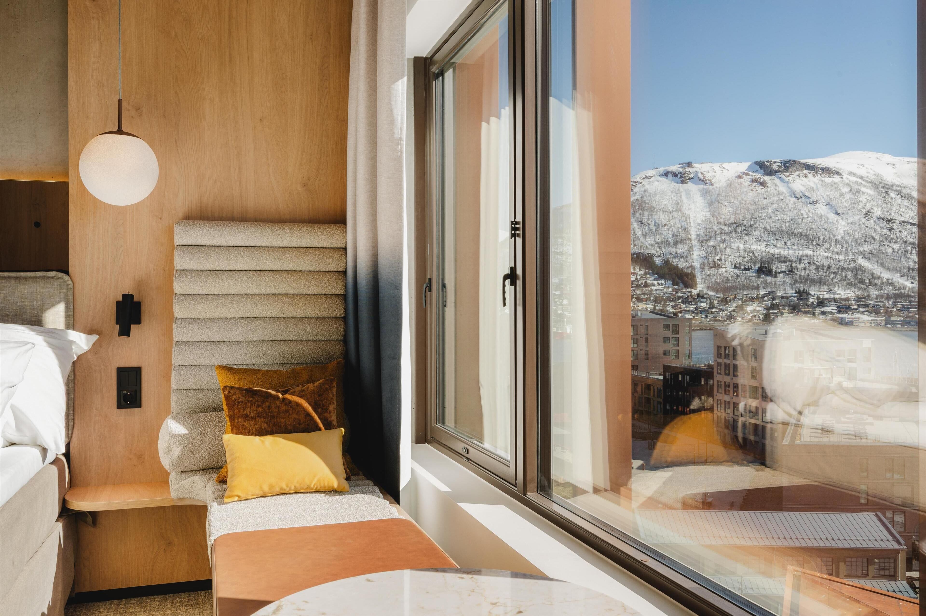 Un interno moderno con un letto, una panca e un'ampia finestra con vista su una montagna innevata.