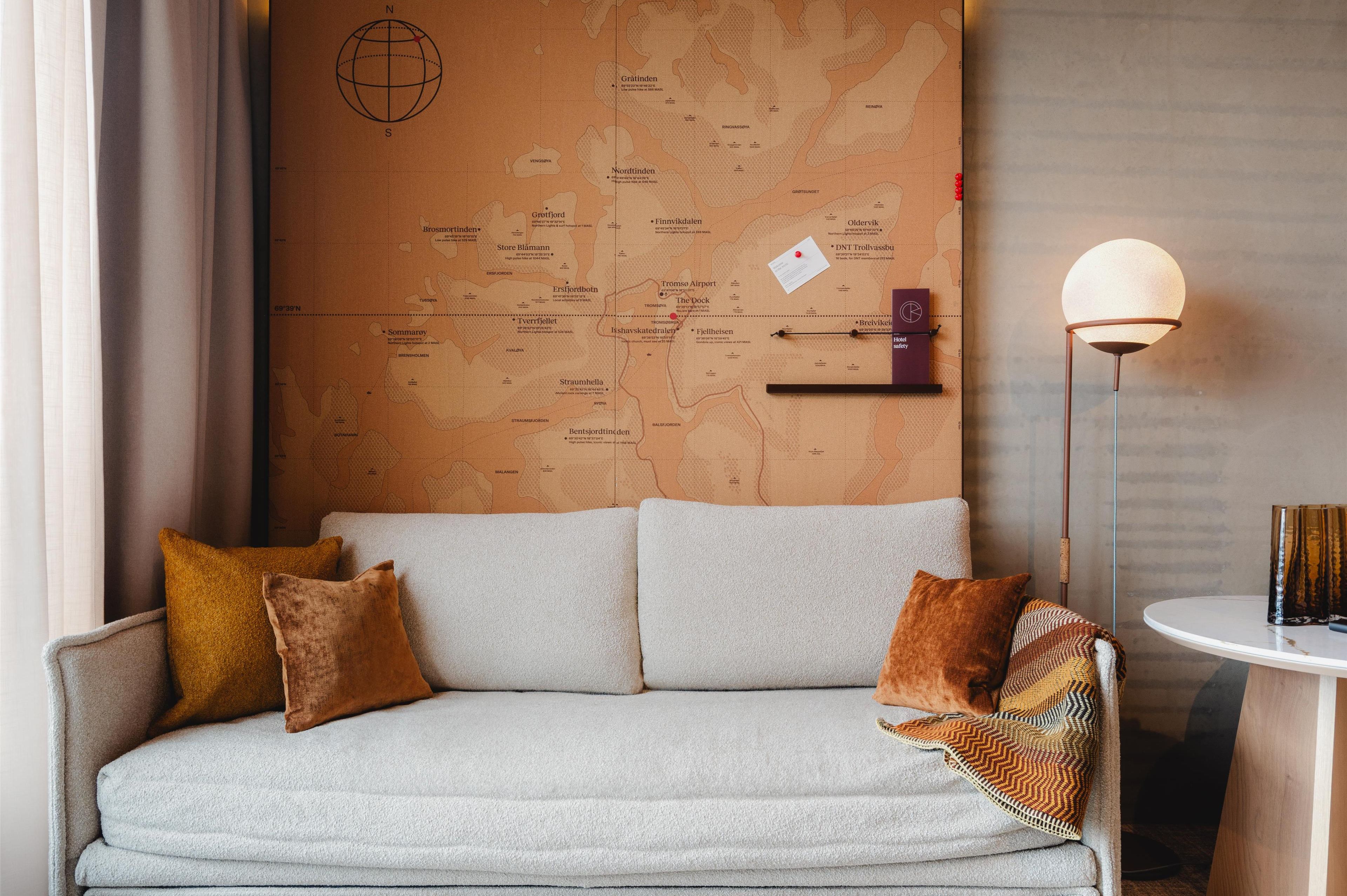 Ein gemütliches Zimmer mit einer Couch, einer Karte an der Wand, einer Lampe und einem kleinen Tisch mit einem Buch.