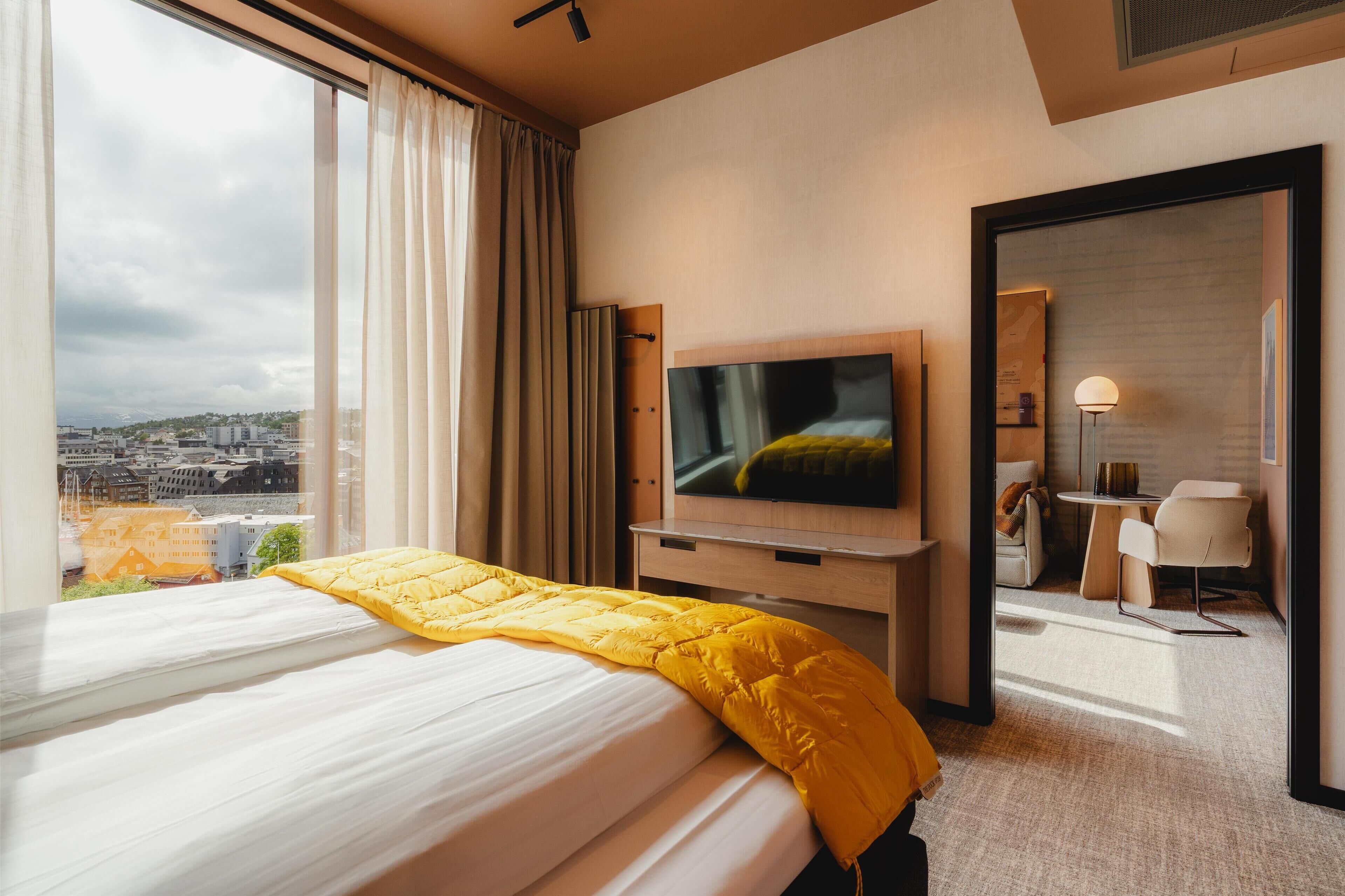 A hotel room with a bed, a TV, a desk, and a view of the city.