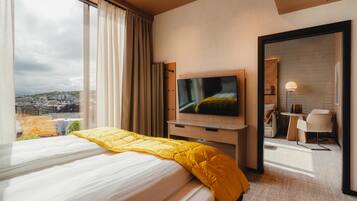 A hotel room with a bed, a TV, a desk, and a view of the city.