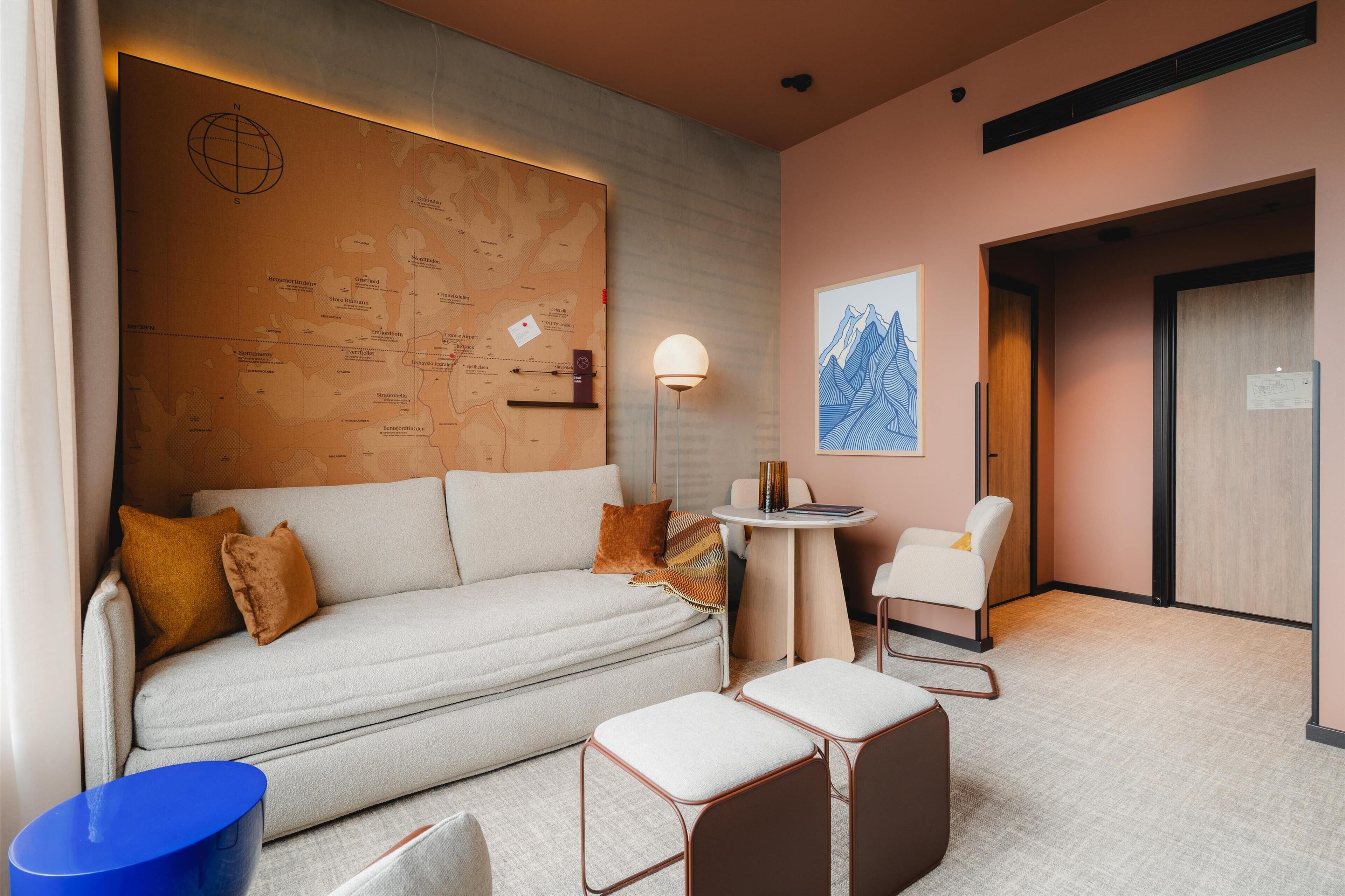 Una habitación de hotel moderna con un sofá, una mesita redonda pequeña, una silla y un mapa en la pared.