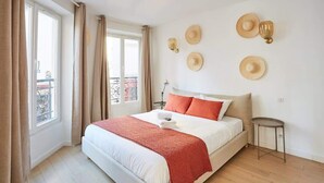 A hotel room with a bed, a bedside table, a window with curtains, and wall-mounted hats. - Sublim Apartment Le Marais Center of Paris (Paris)