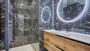 A modern bathroom with a marble backsplash, a wooden vanity, and a large mirror with a circular light. - Apartment in the Center of Paris by studioprestige (Paris)