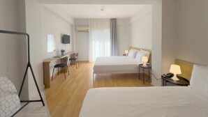 Una habitación de hotel con una cama, mesitas de noche, un escritorio con sillas, un televisor y una ventana con cortinas.
