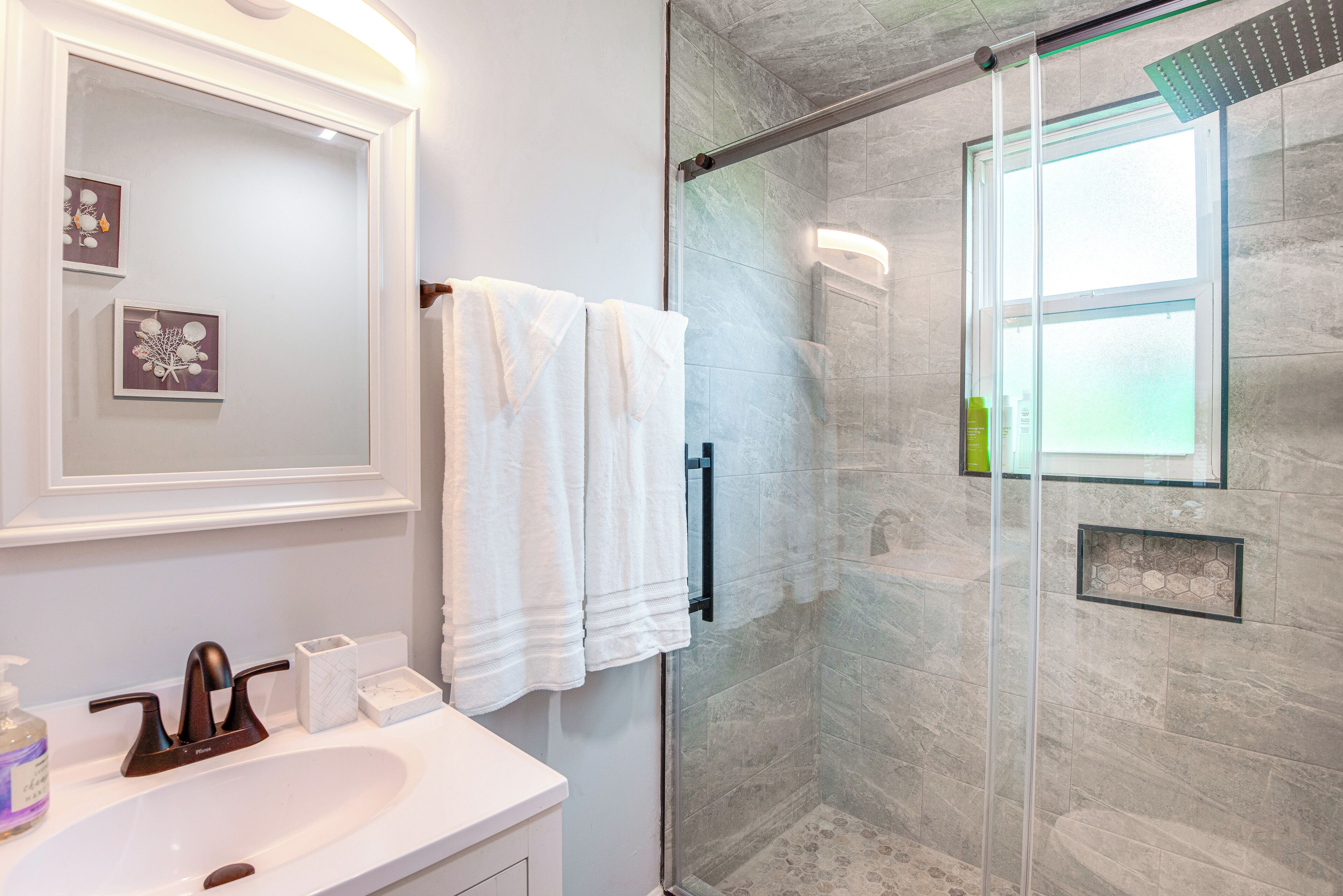 A bathroom with a glass-enclosed shower, a white sink, and a mirror with framed artwork.