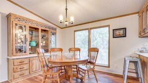 A dining area with a wooden table and chairs, a wooden cabinet with glass doors, and a chandelier. - Relax, Swim & Explore: Home in Wimberley! (Wimberley)