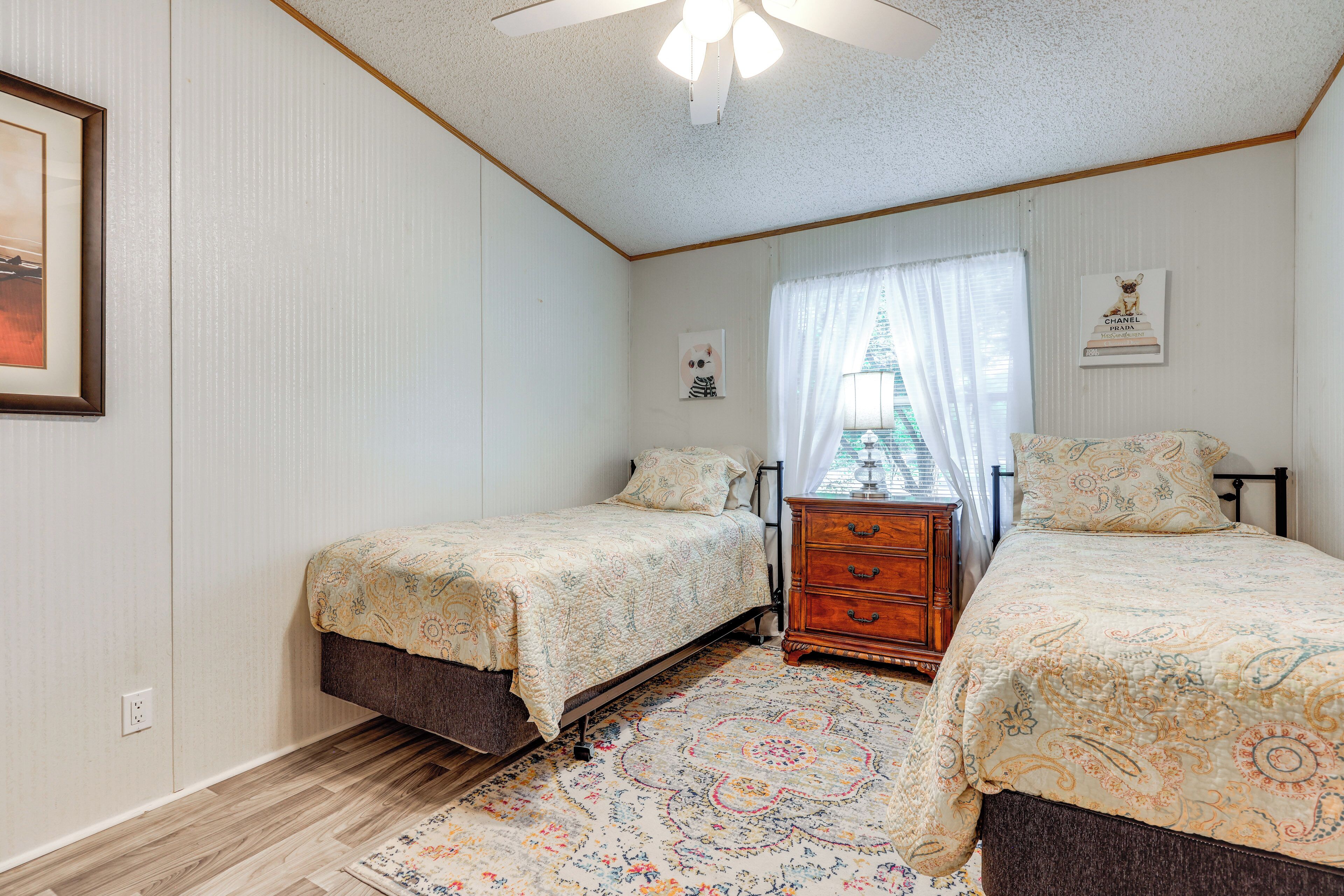 A bedroom with two beds, a wooden dresser, a patterned rug, and a ceiling fan.
