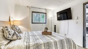 Ett sovrum med en säng, en tv som är monterad på väggen, ett fönster med gardiner och en lampa.