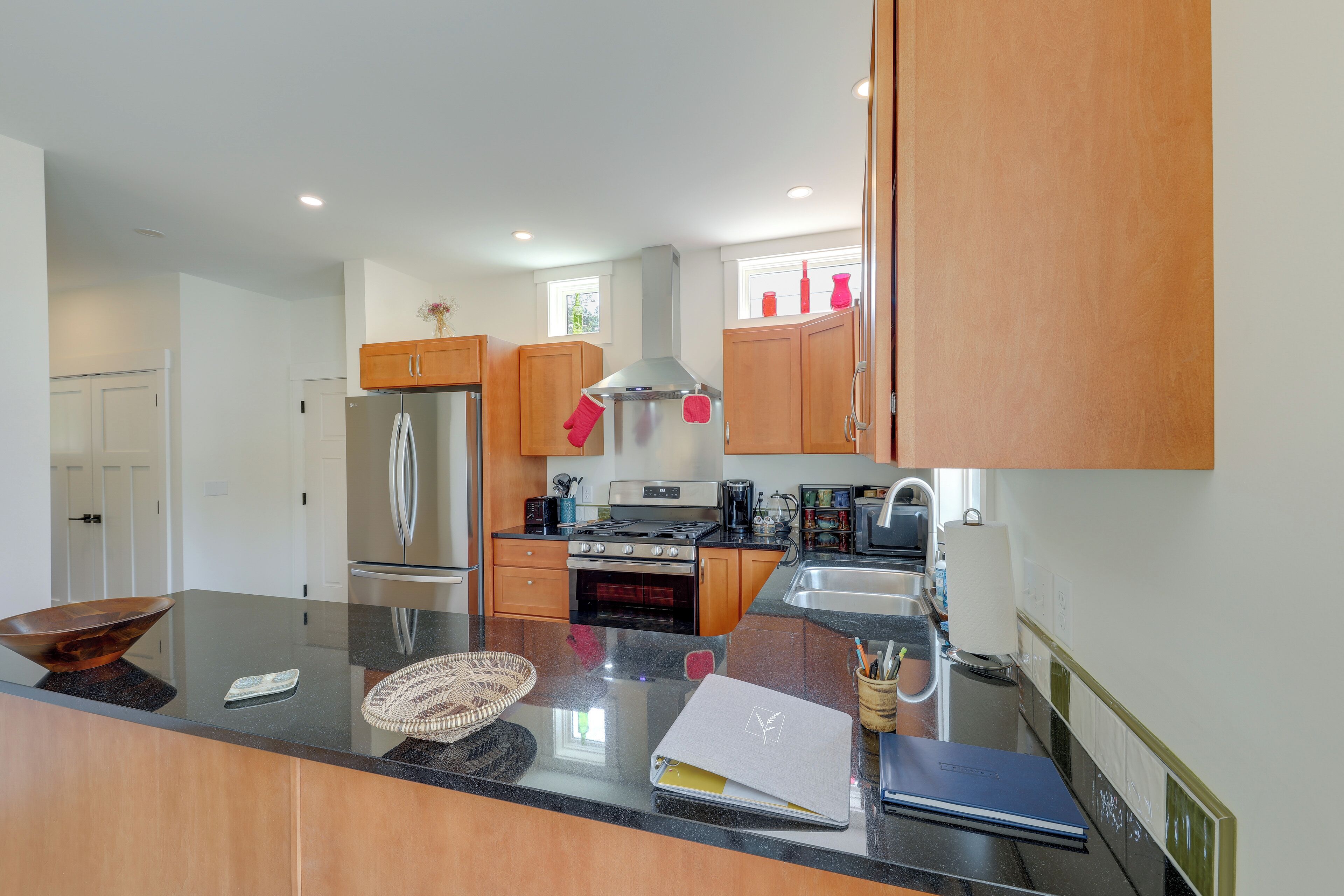 A modern kitchen with wooden cabinets, stainless steel appliances, and a large island with a bowl and notebook.