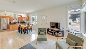 Une cuisine moderne avec des meubles en bois, un coin repas comprenant une table et des chaises, un fauteuil confortable, une bibliothèque et une grande fenêtre donnant sur l’extérieur.
