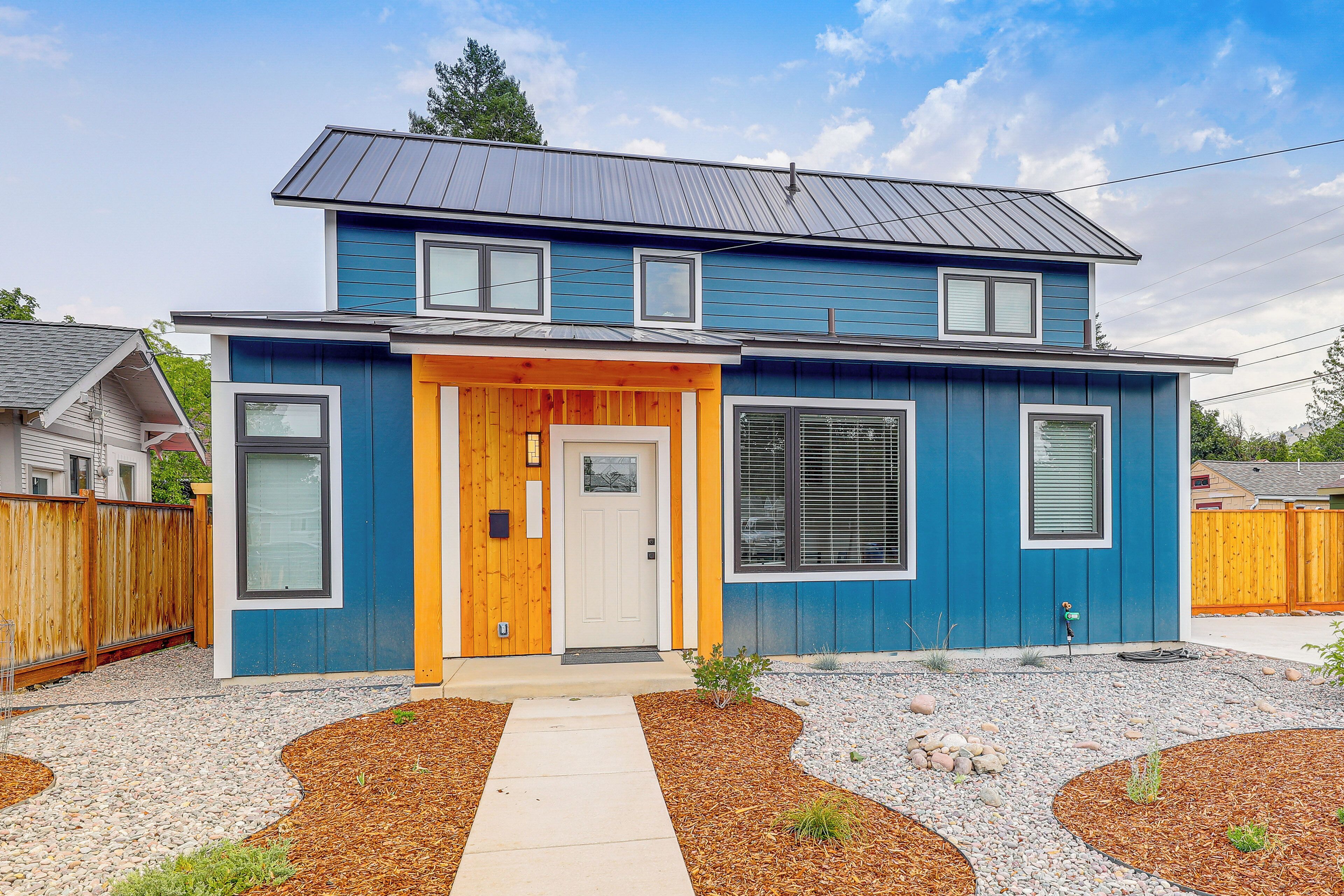 A two-story house with a blue exterior, a front porch, and a driveway leading to the entrance.