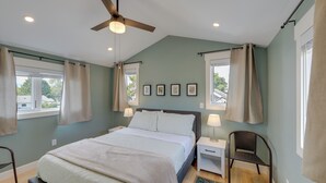 Une chambre à coucher avec un lit, des tables de chevet, une chaise, un ventilateur de plafond et des tableaux encadrés accrochés au mur.