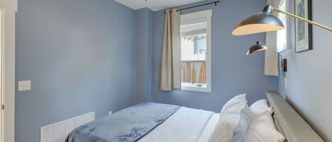 A bedroom with a bed, a ceiling fan, a window with curtains, and a wall-mounted lamp.