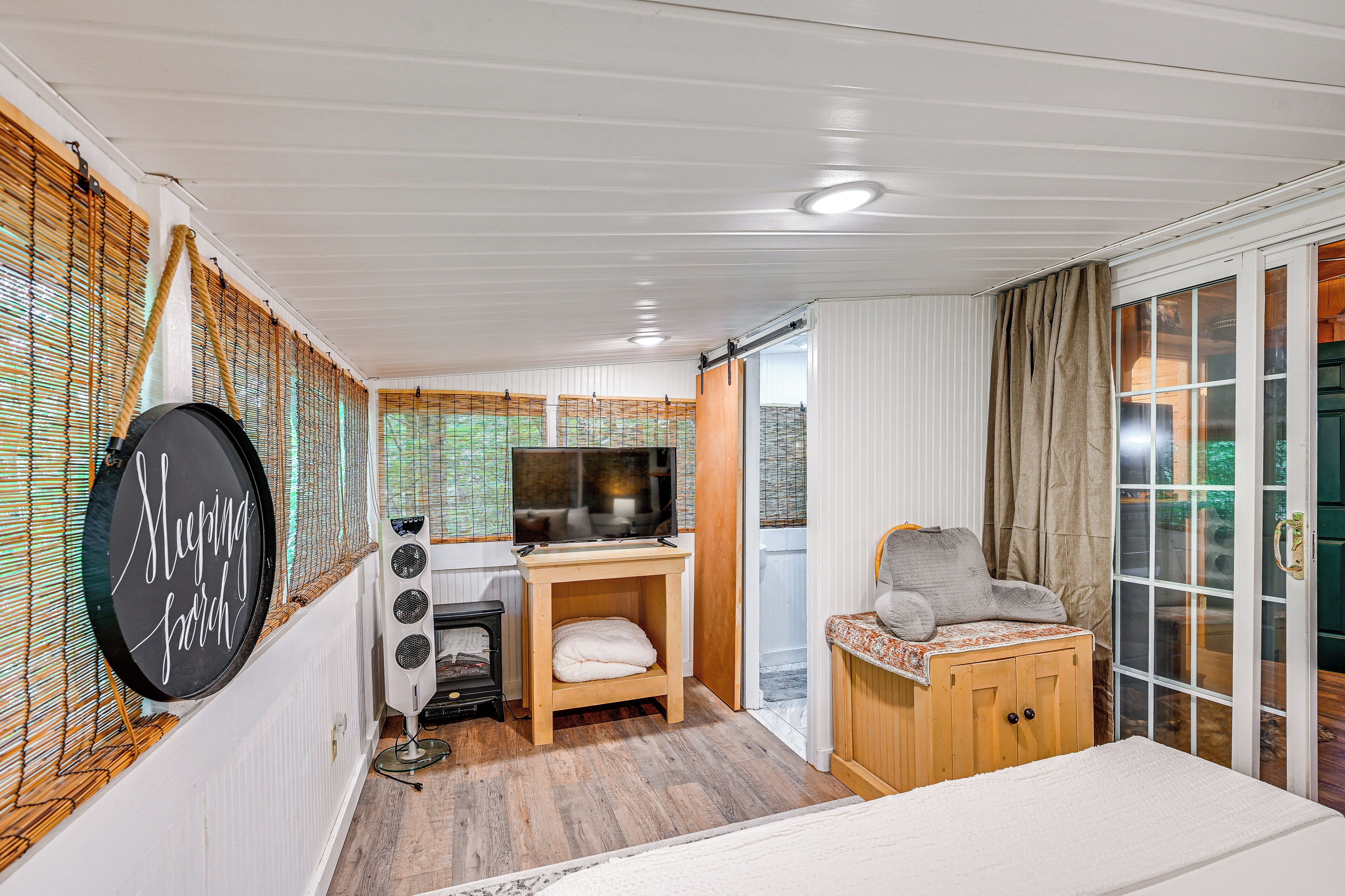 Ein gemütliches Zimmer mit Bett, Fernseher, kleinem Tisch und einem Fenster mit Jalousien.