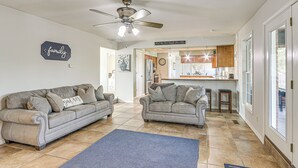 A living room with two grey sofas, a ceiling fan, and a kitchen in the background. - Waterfront Kansas Home w/ Private Fire Pit! (Arkansas City)